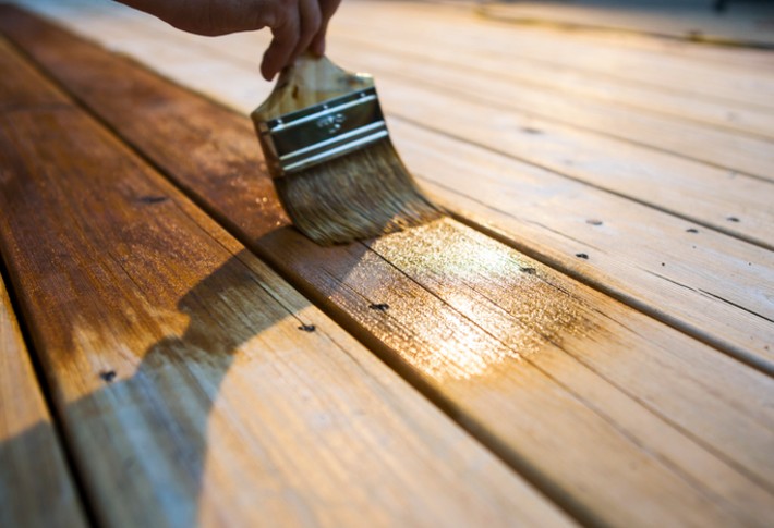 A hand with a brush painting a wooden deck with a stain